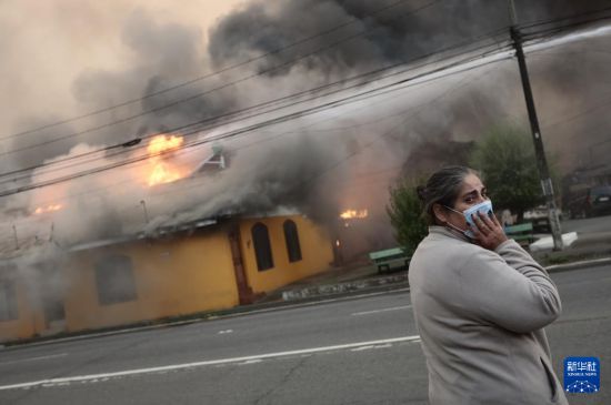 1月18日，在智利比奥比奥大区彭科市，一名女子站在燃烧的建筑前。新华社发